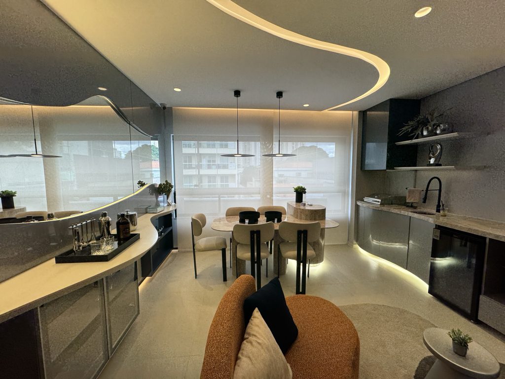 Imagem do apartamento decorado Horizon em Guarulhos, uma área de cozinha moderna, com mesa com cinco lugares, bancada dos dois lados, tudo em tons de cinza, com abacamentos em vidro, estilo tecnológico.