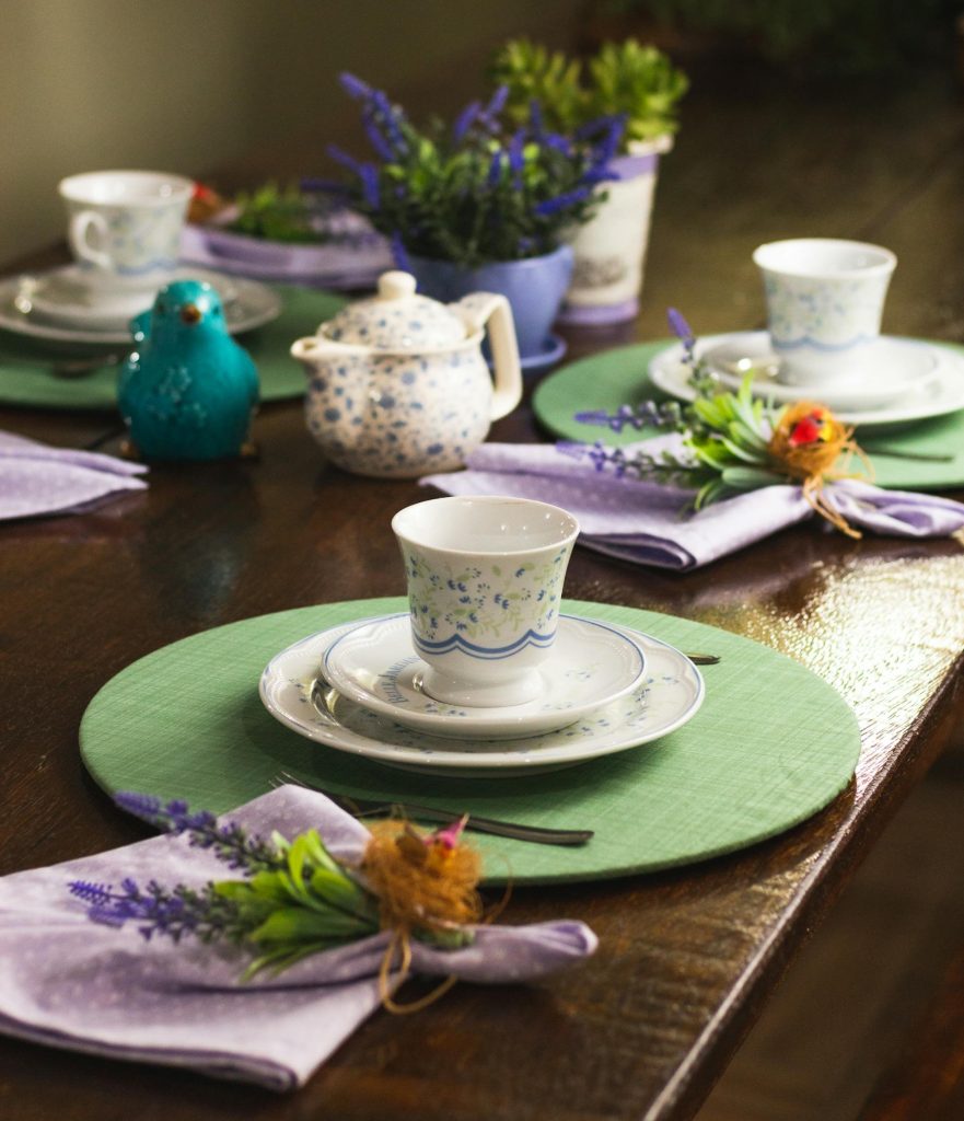 Uma mesa arrumada para uma celebração, com xícaras e pratinhos combinando, ramos de flores e outros detalhes decorativos