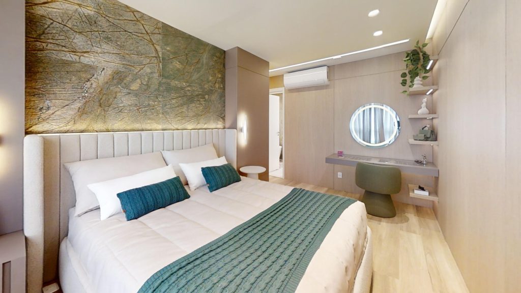 Quarto moderno no AYA, empreendimento de alto padrão em Guarulhos, com uma cama de casal, ar-condicionado penteadeira, espelho e itens de decoração
