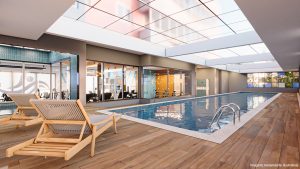 Piscina do AYA, empreendimento de alto padrão em Guarulhos, com deck de madeira e espreguiçadeiras ao redor com um amplo teto de vidro