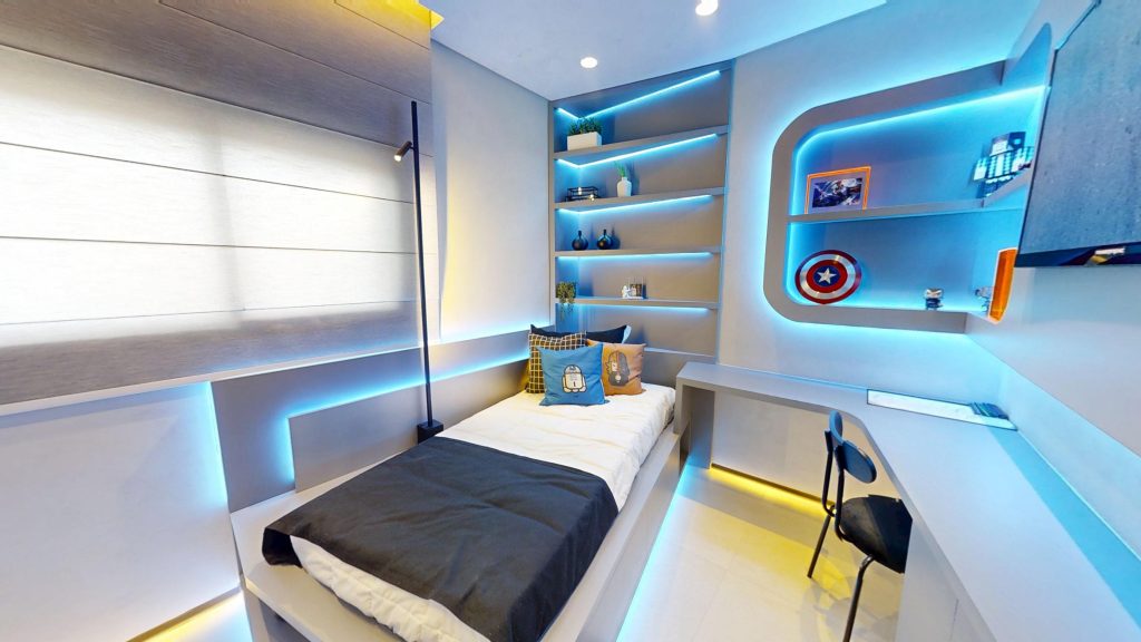Imagem de um apartamento em Guarulhos, trata-se de um quarto em um dos decorados do Horizon, o empreendimento mais tecnológico de Guarulhos, com uma cama de solteiro, mesa de escritorio e prateleiras, todo o ambiente é moderno com decoração futurista e luzes indiretas