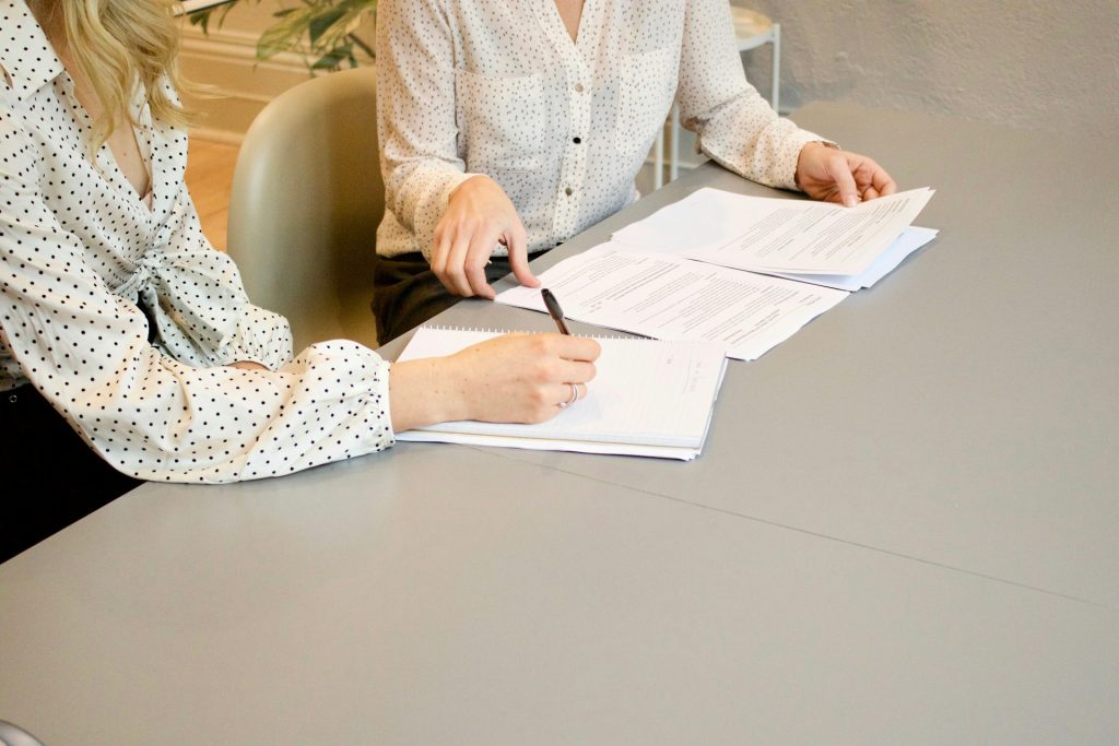 Duas mulheres sentadas em uma mesa com alguns papéis e canetas