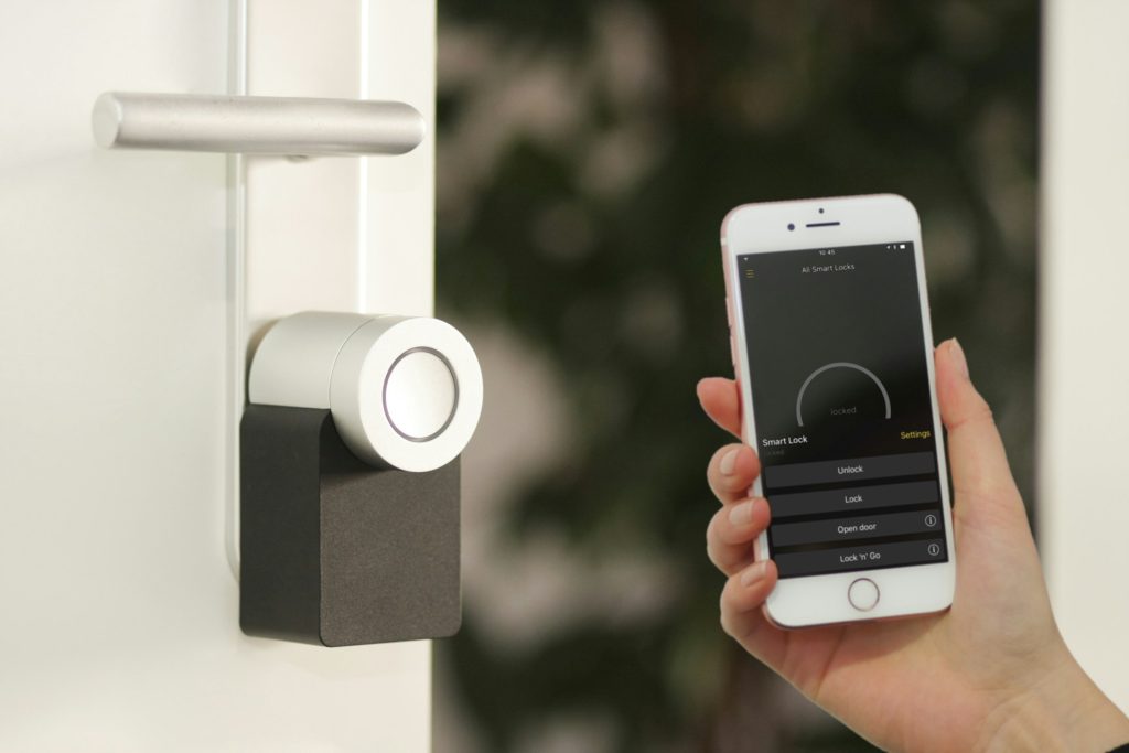 Uma pessoa segurança um celular perto de uma porta com fechadura biométrica, para representar a auotmação residencial presente no Horizon, empreendimento tecnológico em Guarulhos